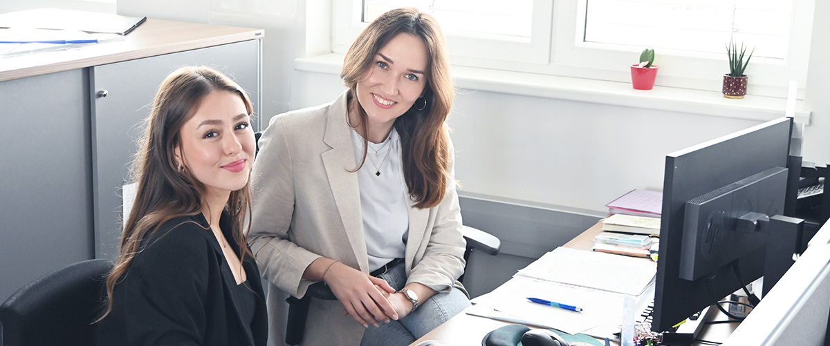 Zwei Frauen besprechen am Arbeitsplatz etwas. Darstellung für die Lehrlingsausbildung Großhandel. 